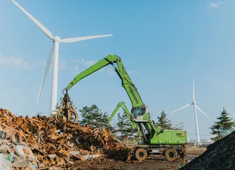 Green material handler lifting scrap metal pile